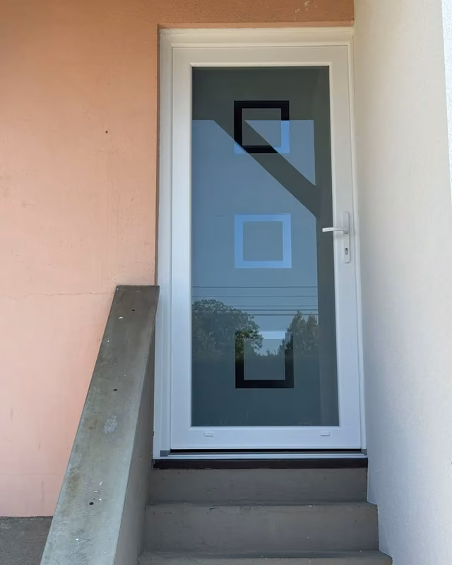 Porte d’entrée blanche à grand vitrage décoré de carrés, en haut d’un escalier — photo de chantier